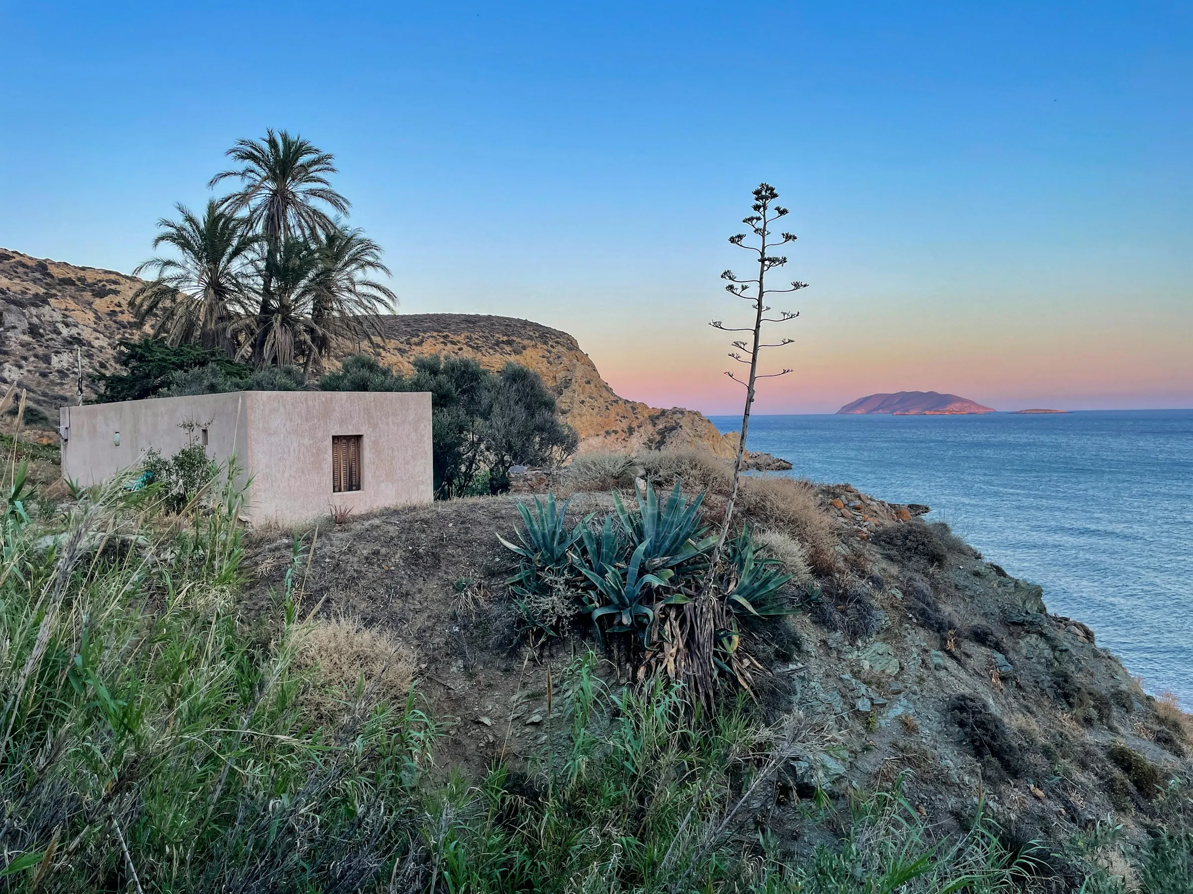 Low whitewashed house on a hillside above the sea